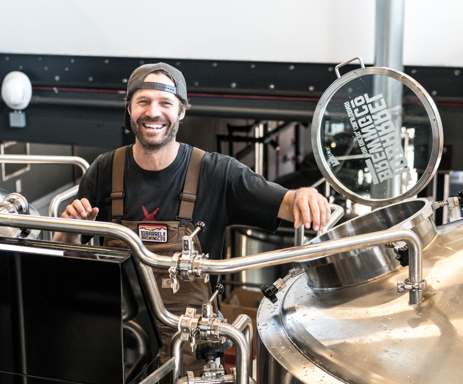 A brewer working at stainless steel tanks on a production floor